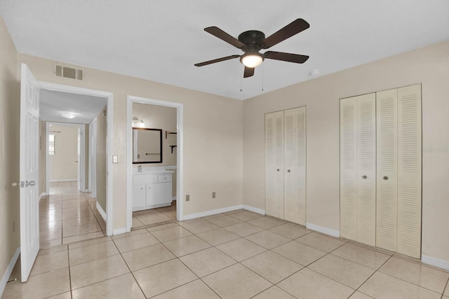 unfurnished bedroom with two closets, ensuite bath, ceiling fan, and light tile patterned flooring