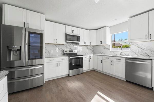 kitchen with sink, appliances with stainless steel finishes, tasteful backsplash, dark hardwood / wood-style flooring, and white cabinetry