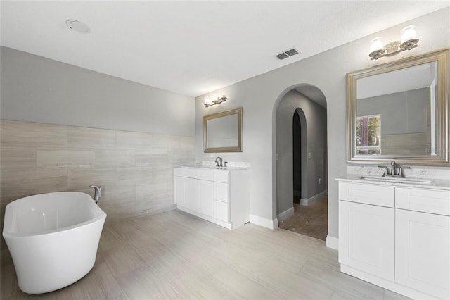 bathroom with vanity, tile walls, and a tub