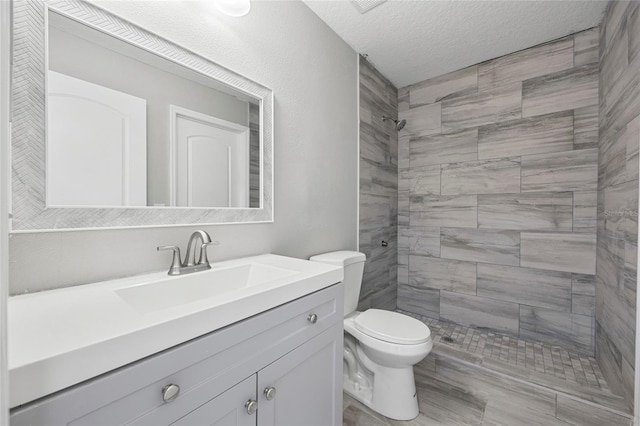 bathroom featuring vanity, toilet, tiled shower, and a textured ceiling