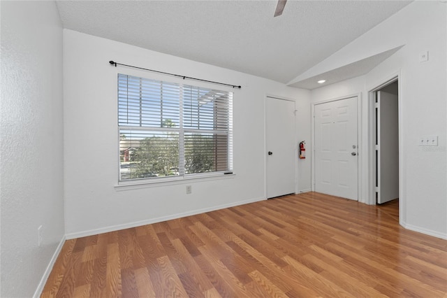 spare room with a textured ceiling, light hardwood / wood-style floors, and lofted ceiling