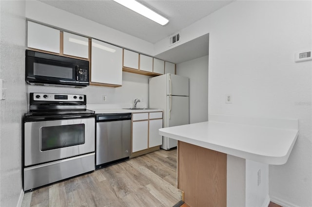 kitchen with white cabinets, light wood-type flooring, stainless steel appliances, and a textured ceiling