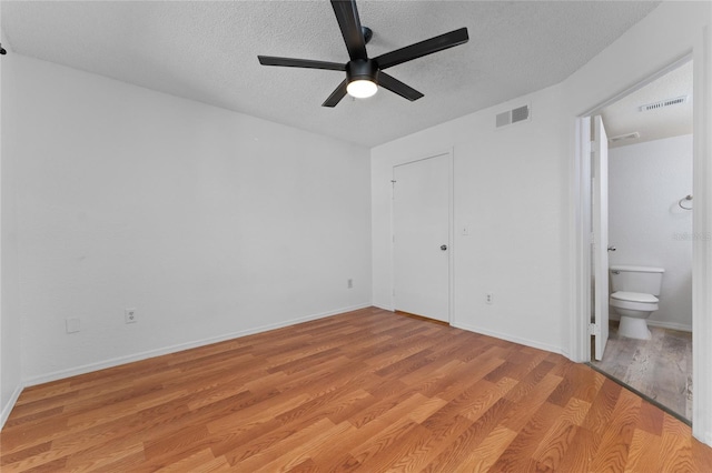 unfurnished bedroom featuring a textured ceiling, ensuite bath, light hardwood / wood-style flooring, and ceiling fan