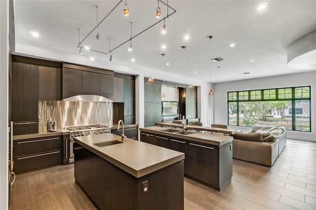 kitchen with dark brown cabinetry, sink, an island with sink, pendant lighting, and high end stainless steel range