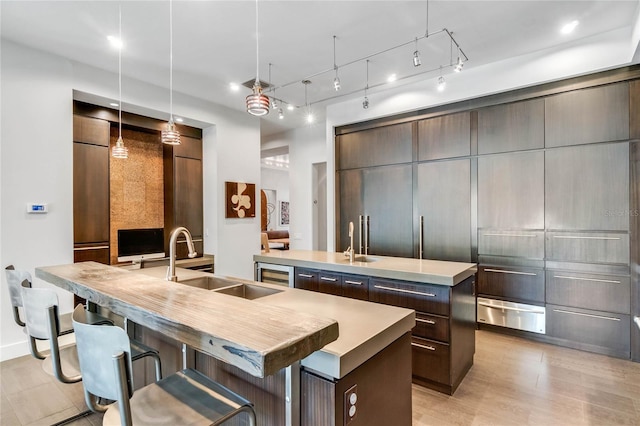 kitchen featuring a center island with sink, dark brown cabinets, sink, and hanging light fixtures