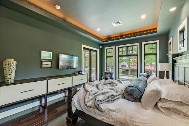 bedroom with a fireplace, dark hardwood / wood-style flooring, a raised ceiling, and multiple windows