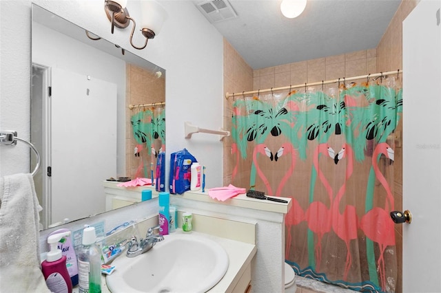 bathroom featuring a textured ceiling, vanity, toilet, and walk in shower