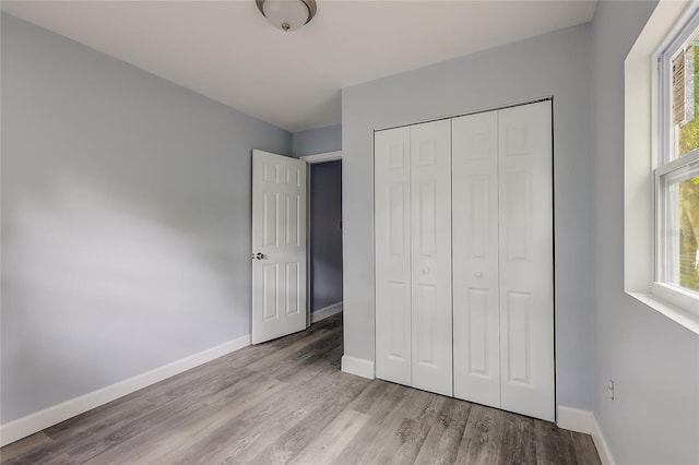 unfurnished bedroom featuring light wood-type flooring, a closet, and multiple windows