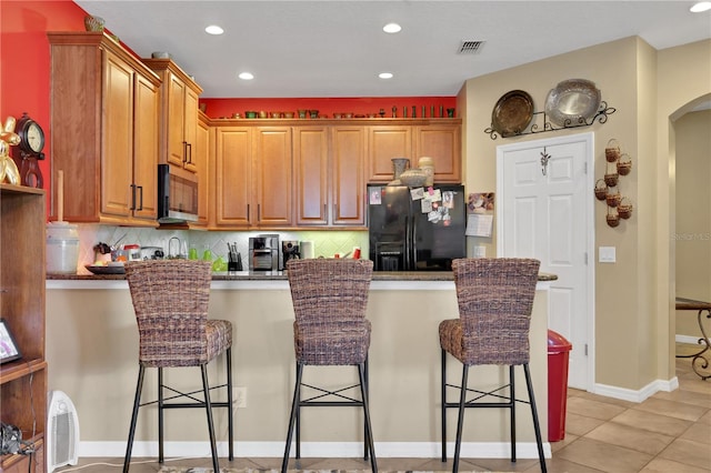 kitchen with a breakfast bar, light tile patterned floors, backsplash, and black fridge