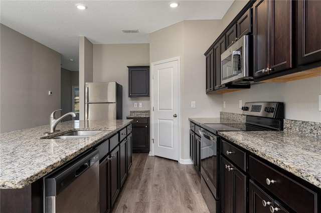 kitchen with light stone countertops, sink, stainless steel appliances, light hardwood / wood-style flooring, and a kitchen island with sink