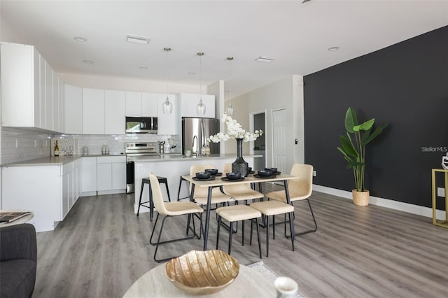 kitchen with stainless steel appliances, tasteful backsplash, pendant lighting, white cabinets, and light wood-type flooring