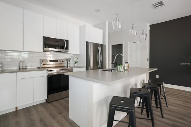 kitchen with appliances with stainless steel finishes, dark hardwood / wood-style flooring, sink, a center island with sink, and hanging light fixtures