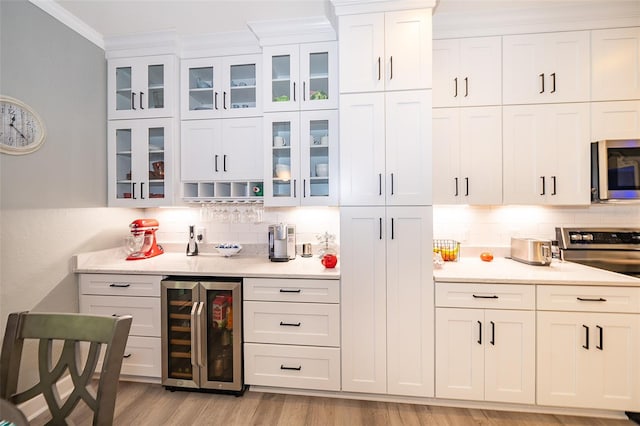 bar with light hardwood / wood-style flooring, white cabinetry, beverage cooler, and crown molding