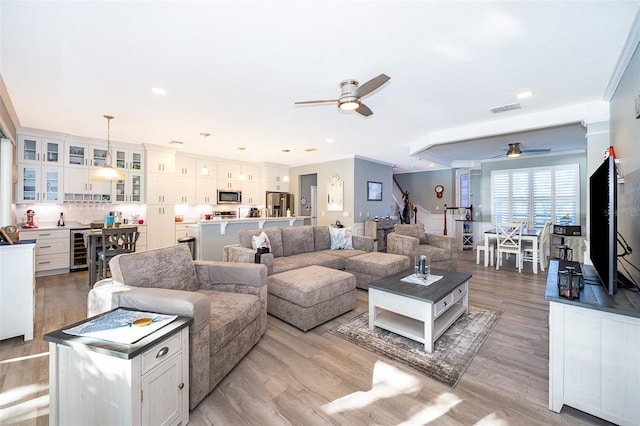 living room with ceiling fan, beverage cooler, light hardwood / wood-style floors, and ornamental molding