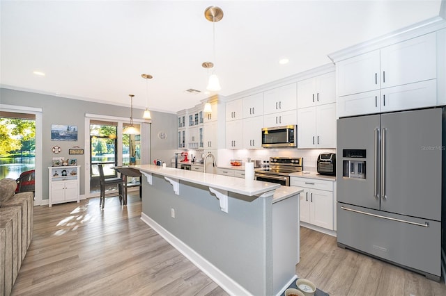 kitchen with a breakfast bar, white cabinets, hanging light fixtures, light hardwood / wood-style flooring, and stainless steel appliances