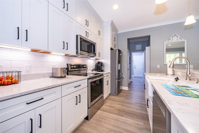 kitchen with white cabinets, hanging light fixtures, ornamental molding, light hardwood / wood-style floors, and stainless steel appliances