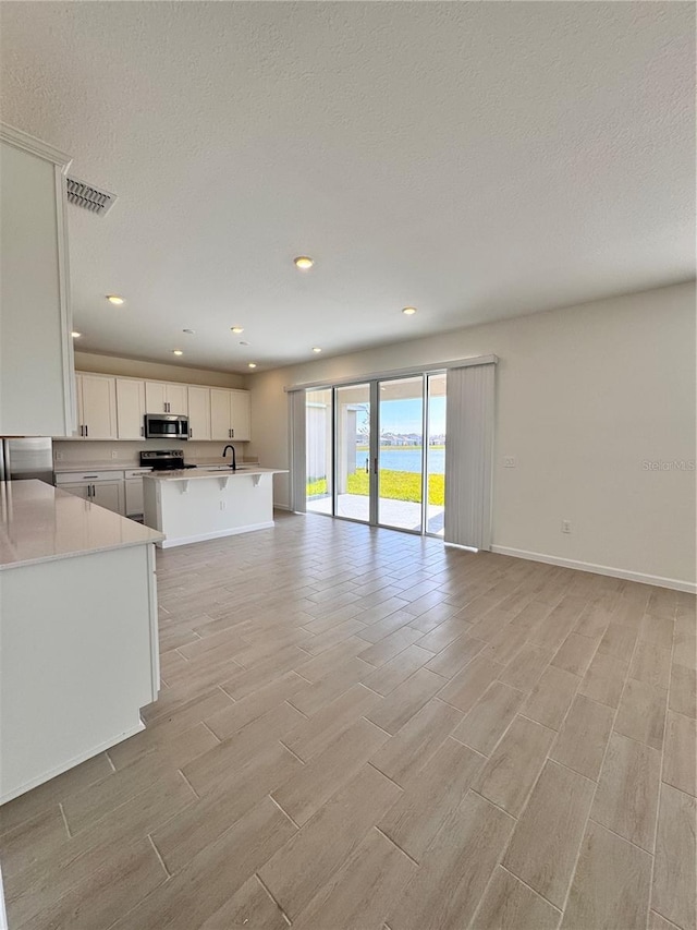 unfurnished living room with a textured ceiling, light wood-type flooring, and sink