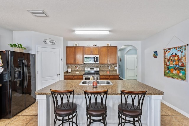 kitchen with stainless steel appliances, a kitchen breakfast bar, a textured ceiling, a kitchen island with sink, and light tile patterned flooring