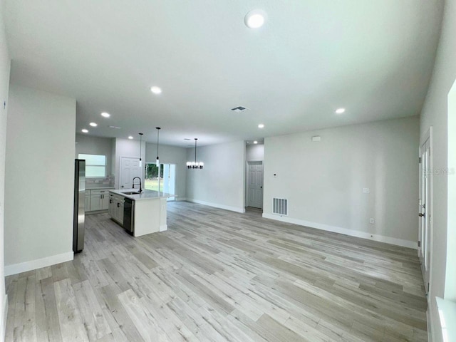 kitchen featuring decorative light fixtures, light wood-type flooring, a kitchen island with sink, and stainless steel refrigerator