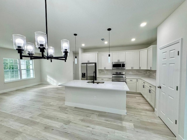 kitchen featuring stainless steel appliances, a kitchen island with sink, sink, white cabinetry, and hanging light fixtures