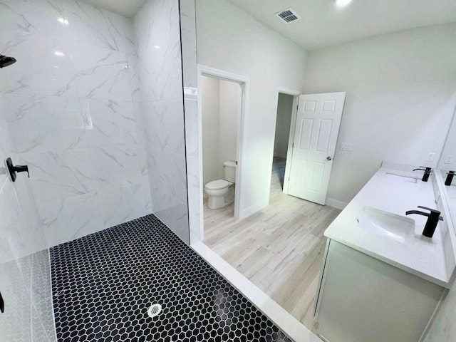 bathroom with a tile shower, hardwood / wood-style floors, vanity, and toilet