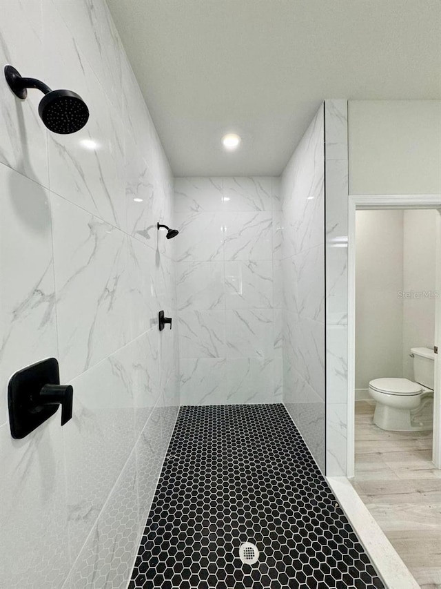 bathroom featuring a tile shower, wood-type flooring, and toilet