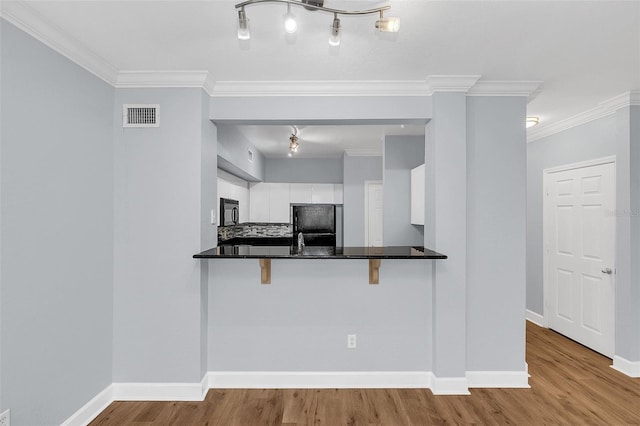204 E S St Unit 1055, Orlando, FL 32801 - kitchen featuring white cabinets, black microwave, fridge, a breakfast bar, and wood finished floors