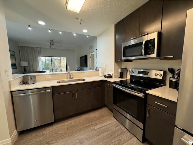 kitchen with light wood-type flooring, a textured ceiling, stainless steel appliances, dark brown cabinetry, and sink