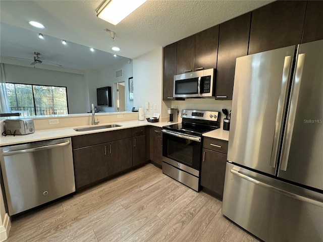 kitchen with ceiling fan, sink, stainless steel appliances, a textured ceiling, and light wood-type flooring