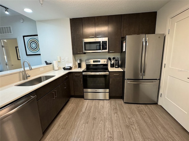 kitchen featuring appliances with stainless steel finishes, a textured ceiling, light hardwood / wood-style flooring, and sink