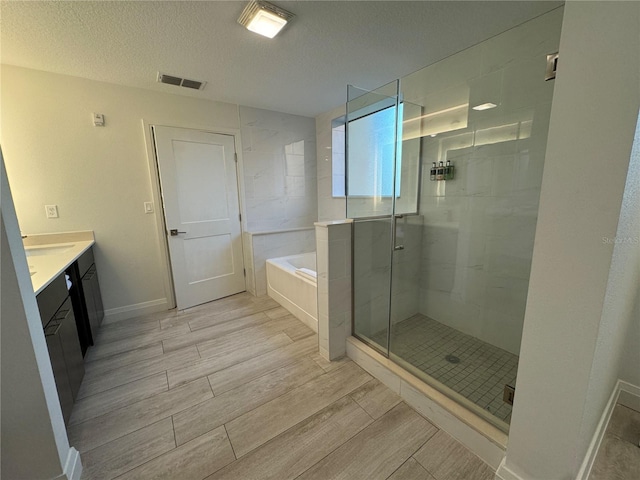 bathroom with a textured ceiling, vanity, and shower with separate bathtub