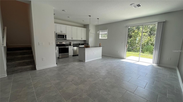 kitchen with appliances with stainless steel finishes, a textured ceiling, white cabinets, a center island, and hanging light fixtures