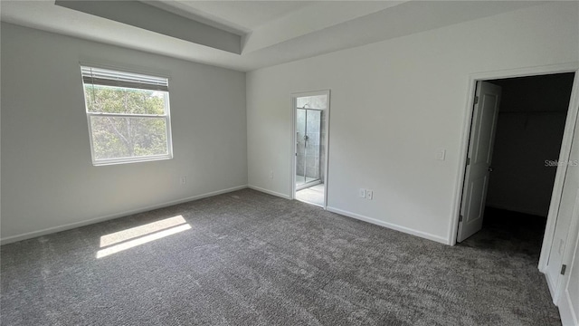 unfurnished bedroom with dark carpet, a spacious closet, and ensuite bath