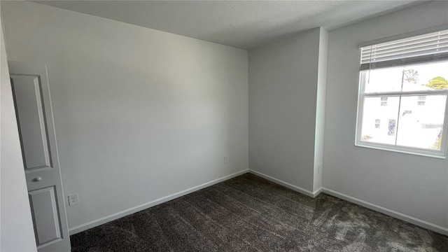 unfurnished room with plenty of natural light, a textured ceiling, and dark colored carpet