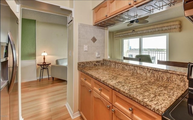 kitchen with stainless steel fridge, stove, tasteful backsplash, light stone counters, and light hardwood / wood-style floors