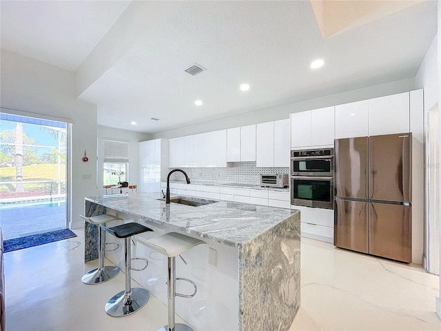 kitchen with white cabinetry, sink, stainless steel appliances, tasteful backsplash, and a kitchen island with sink