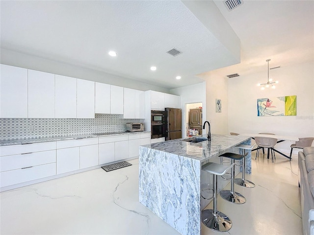 kitchen with white cabinetry, sink, hanging light fixtures, backsplash, and a center island with sink