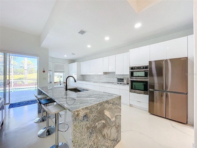 kitchen featuring sink, an island with sink, appliances with stainless steel finishes, tasteful backsplash, and white cabinetry