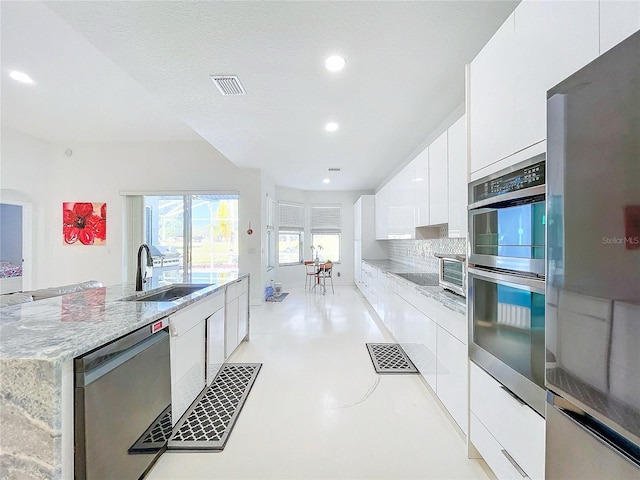 kitchen featuring appliances with stainless steel finishes, backsplash, light stone counters, sink, and white cabinetry