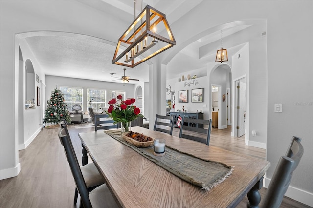 dining space with a textured ceiling, wood-type flooring, and ceiling fan with notable chandelier