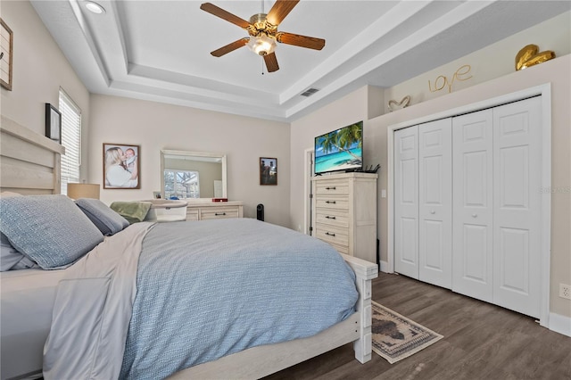 bedroom featuring dark hardwood / wood-style flooring, a closet, a raised ceiling, and ceiling fan