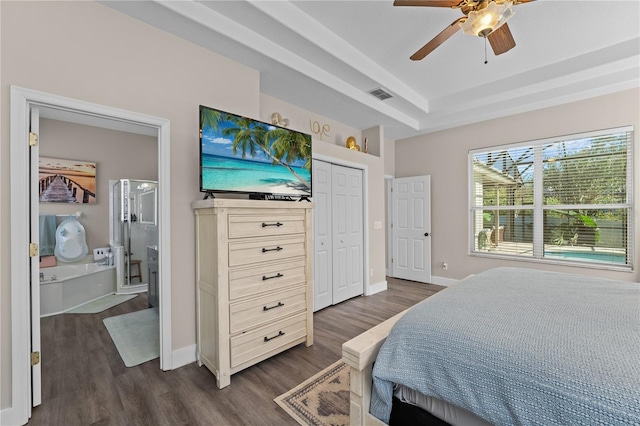 bedroom featuring ensuite bath, a tray ceiling, ceiling fan, dark wood-type flooring, and a closet