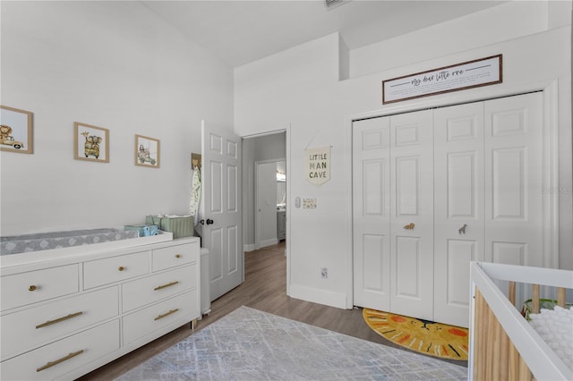 bedroom featuring lofted ceiling, a crib, wood-type flooring, and a closet