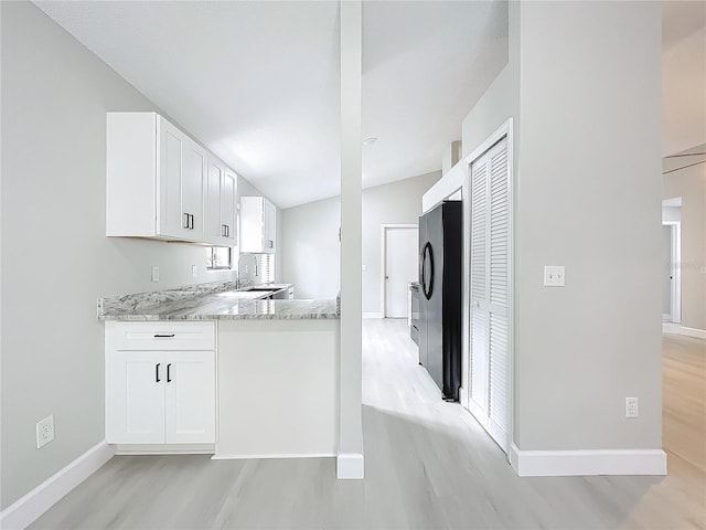 kitchen with white cabinets, light wood-type flooring, vaulted ceiling, and light stone counters