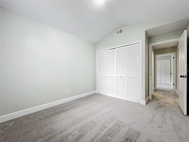 unfurnished bedroom featuring a textured ceiling, light carpet, a closet, and vaulted ceiling