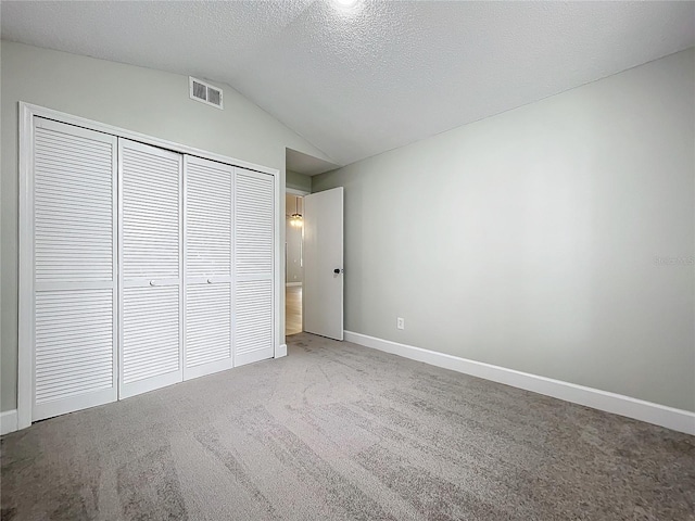 unfurnished bedroom featuring carpet flooring, a closet, a textured ceiling, and lofted ceiling