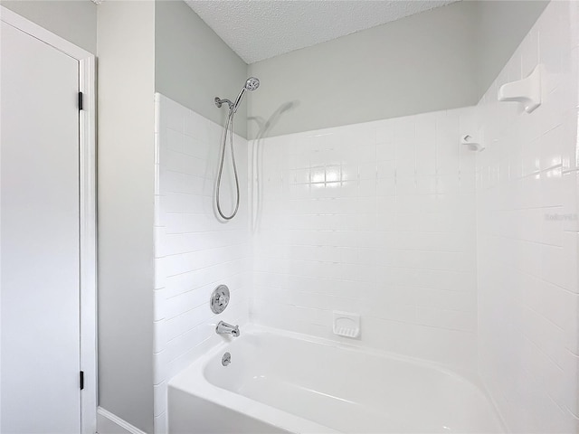 bathroom with a textured ceiling and tiled shower / bath