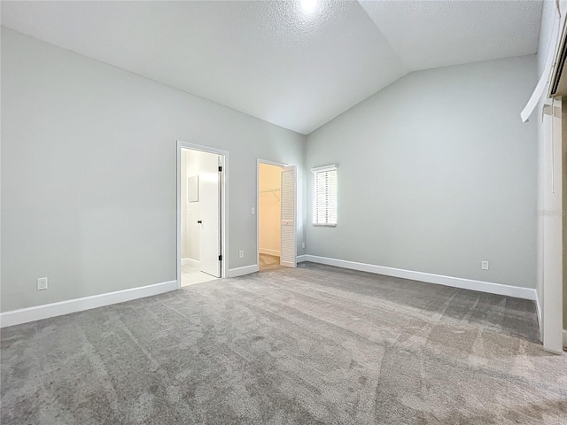 unfurnished bedroom with a textured ceiling, vaulted ceiling, a walk in closet, a closet, and carpet