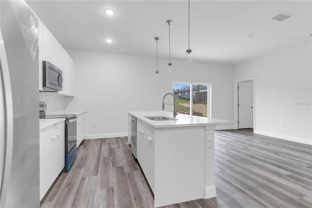 kitchen with sink, a center island with sink, pendant lighting, stainless steel appliances, and white cabinets