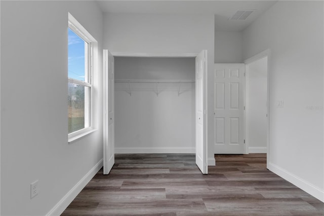 unfurnished bedroom with hardwood / wood-style flooring, a closet, and multiple windows